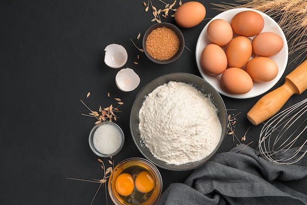 Baking, flour, eggs, sugar, rolling pin on a black background with space to copy. Culinary background. Top view.