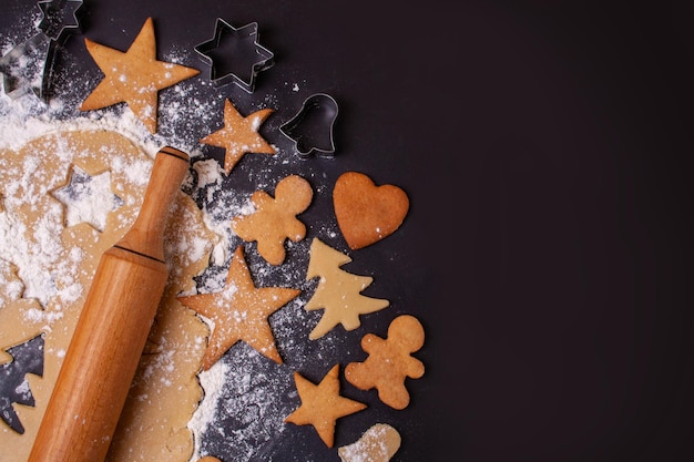 Baking gingerbread cookies on a black background. Dough, flour, gingerbread man. Flat lay style