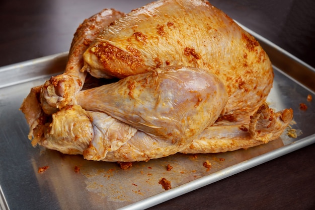 Baking sheet with raw marinated turkey on wooden table.