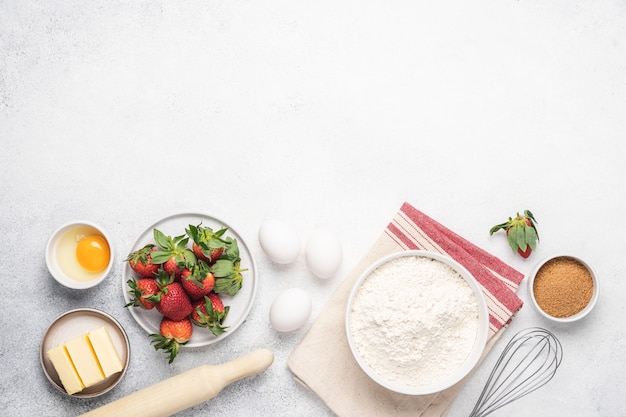 Baking strawberry pie white background. Flour, butter, eggs and kitchen utensils on white stone table