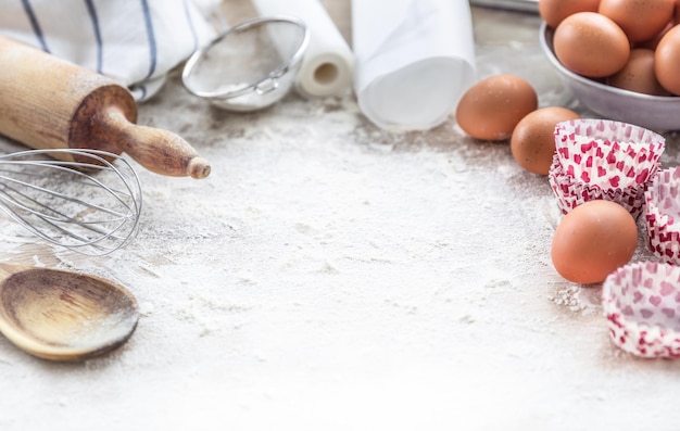 Baking utensils with eggs flour and cupcake cases on kitchen table with copy space.