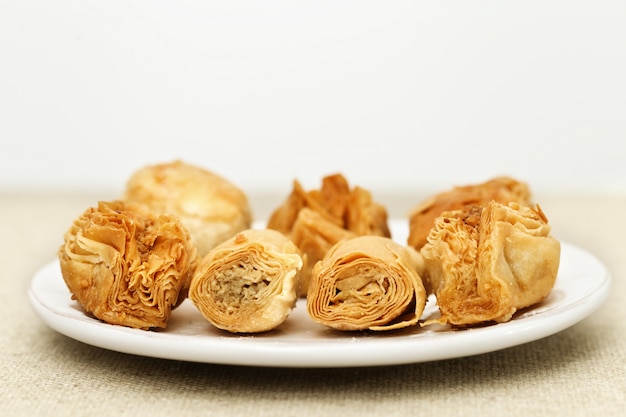 Baklava made of thin dough with chopped nuts and honey syrup on the table on a light background. Selective focus. Copy space.