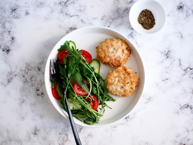 Balanced dinner of two chicken meatballs vegetables salad of rucolla cucumbers tomatoes for diet food light background