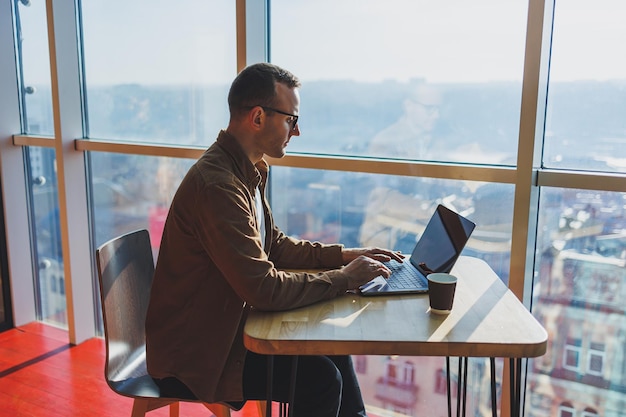 A balanced man in glasses and casual clothes works on a laptop from a cozy workspace A successful freelancer works remotely