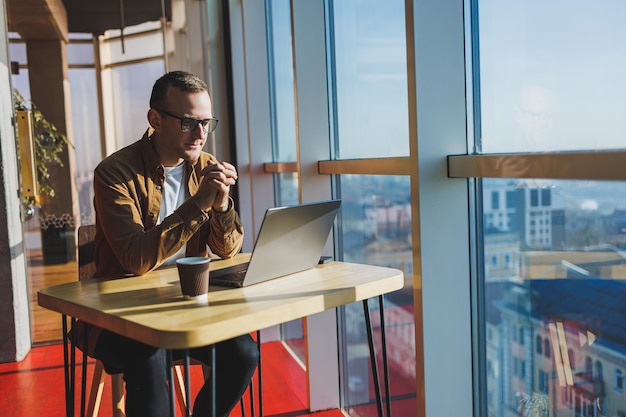 A balanced man in glasses and casual clothes works on a laptop from a cozy workspace A successful freelancer works remotely