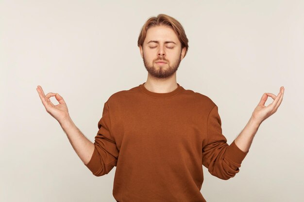 Balanced mind relaxation Portrait of peaceful man with beard in sweatshirt standing calm down with namaste gesture