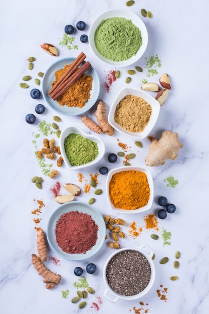 Balanced nutrition concept for clean eating antioxidant detox diet. Assortment of superfood powder - acai, turmeric, wheat, ginger, cinnamon, matcha. Flat lay marble background