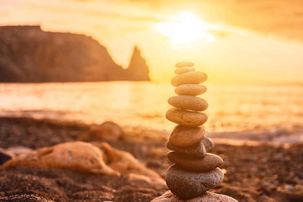 Balanced pebble pyramid on the beach on a sunset time sea waves and foam on the background selective