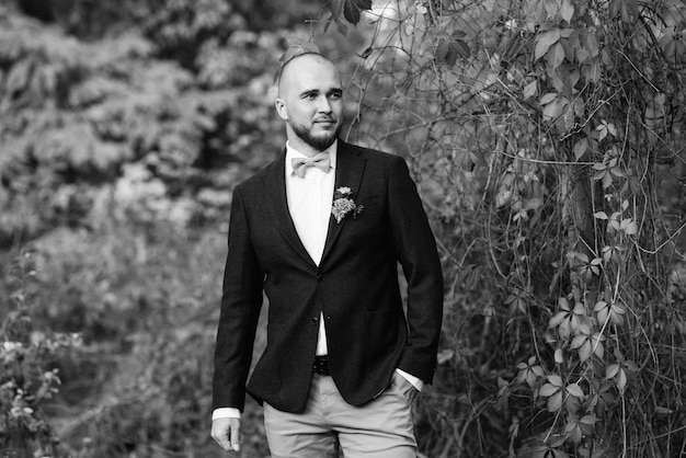 Bald bearded guy in a brown jacket on a background of red wild grapes