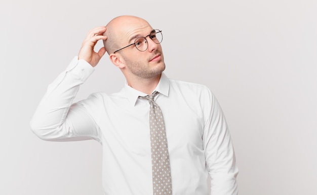 Bald businessman feeling puzzled and confused, scratching head and looking to the side