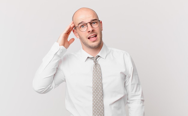 Bald businessman looking happy, astonished and surprised, smiling and realizing amazing and incredible good news