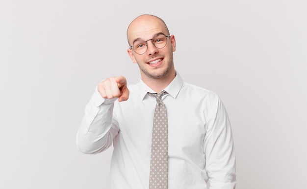 Bald businessman pointing at front with a satisfied, confident, friendly smile, choosing you