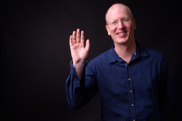 bald businessman with eyeglasses against black wall