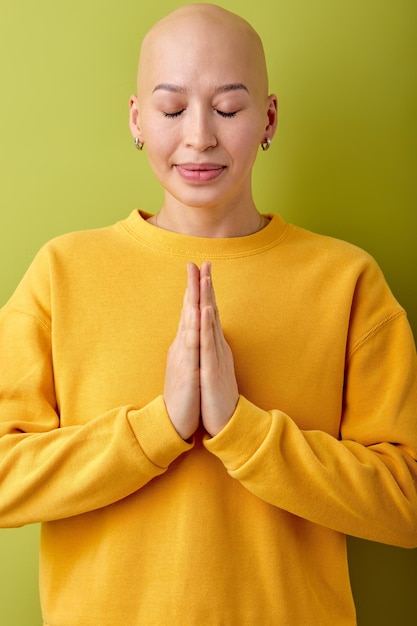 Bald lady folding hands in prayer position isolated green studio background