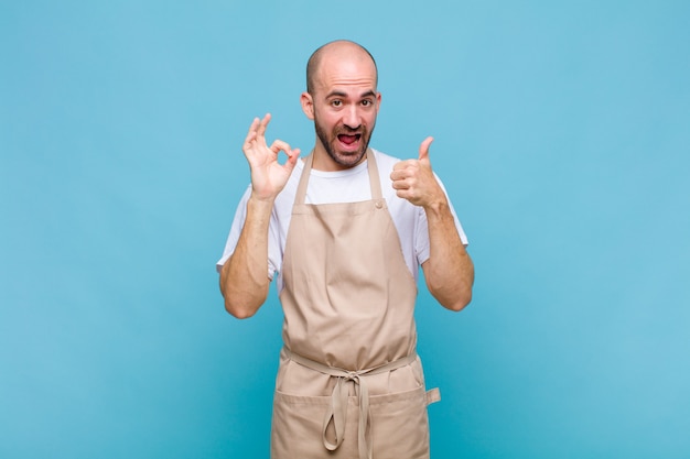 Bald man feeling happy, amazed, satisfied and surprised, showing okay and thumbs up gestures, smiling