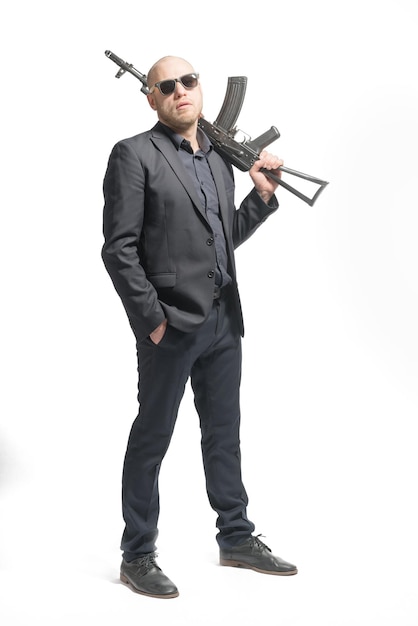 Bald man in a gray suit and sunglasses holding a machine gun on his shoulder Isolated