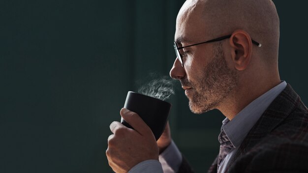 Photo bald man holding a mug of hot drink and sniffing it