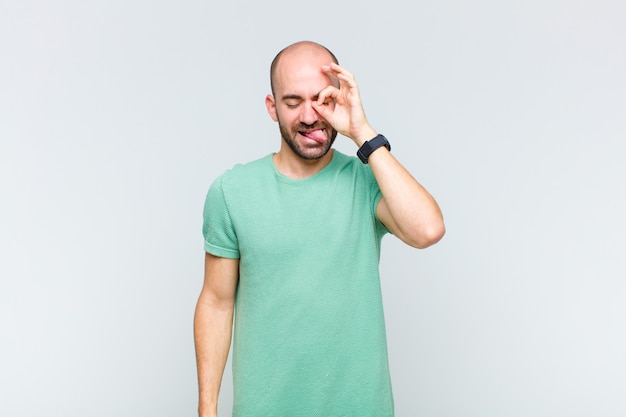 Bald man smiling happily with funny face, joking and looking through peephole, spying on secrets