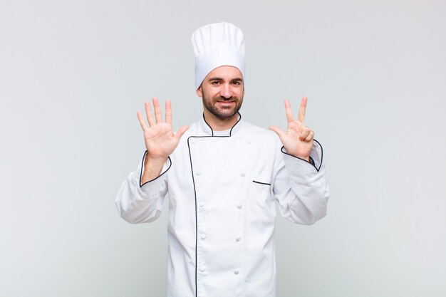 Bald man smiling and looking friendly, showing number eight or eighth with hand forward, counting down