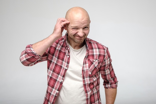 Bald man with stubble on face looks into camera with repentance smiles guiltily and narrows eye