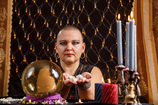 A bald woman fortune teller reads the future on runes by candlelight in a saloon