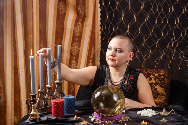 A bald woman fortuneteller lights candles in a magic salon horizontal photo