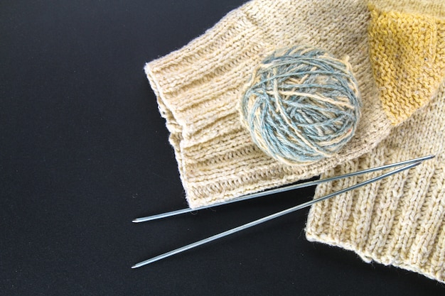 A ball of wool with knitting needles and socks on a gray table. Needlework