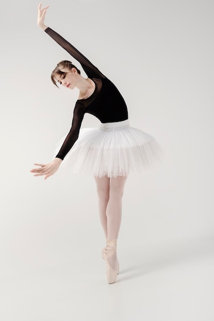 Ballerina in a black bodysuit and tutu poses in motion showing elements while standing on pointe