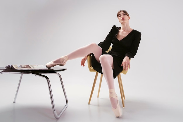 Ballerina in a black dress sits sexy at a coffee table with her legs folded on it in punts