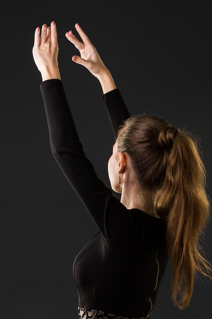 Ballerina dancer posing with her hands on a dark background