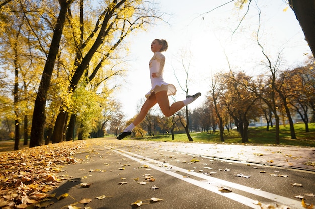 Ballerina dancing in nature park among autumn leaves.