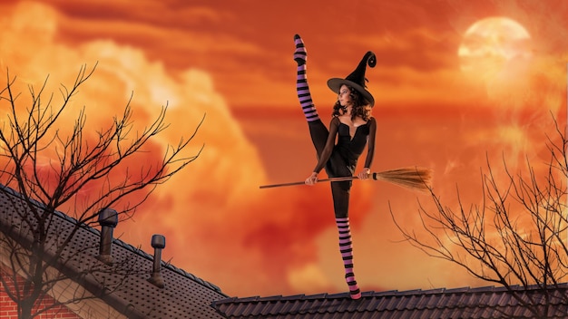 A ballerina in pointe shoes in a black witch costume with a hat and a broom is dancing on the roof of an old house against the backdrop of an ominous bright sunset