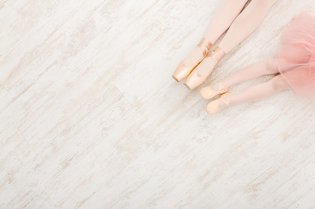 Ballet background. Little girl and young ballerina legs in pointe shoes on white wooden floor, top view from above with copy space. Classical dance school background, practicing for children