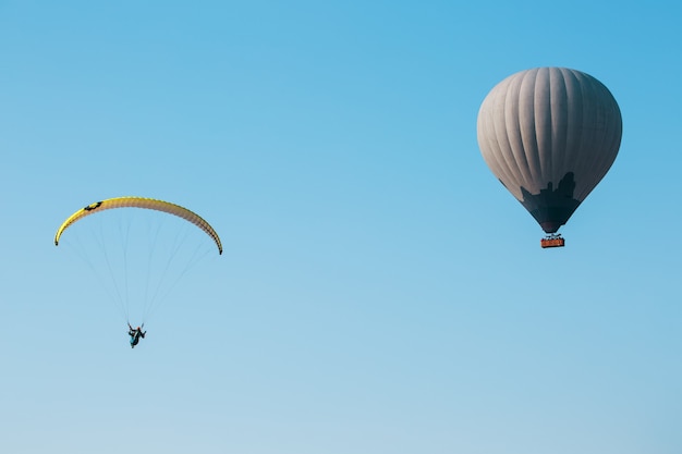 Balloon and paraglider soars against the blue sky.