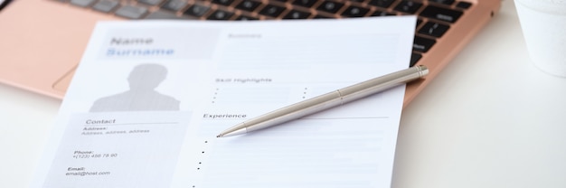 Ballpoint pen lying on resume document for employment near laptop closeup