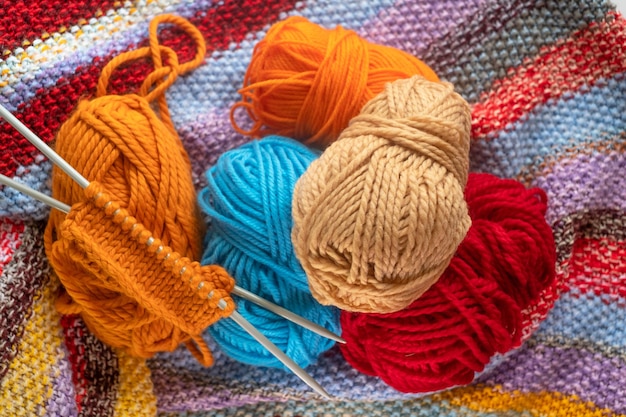 Balls of colored yarn. Knitting project in progress. A piece of knitting with orange ball of yarn and a knitting needles.