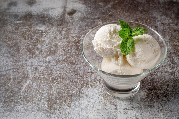 Balls of vanilla cream ice cream with mint in a glass against a backdrop of gray stone. Summer dessert.