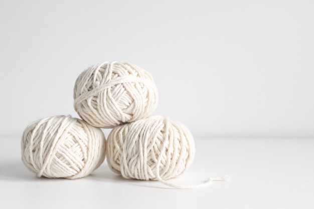 Balls of white yarn on a white wall background. Threads of wool boho image. Space for text. Good for macrame and handicrafts banners and advertisement