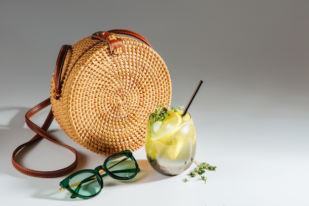 Bamboo bag with sunglasses and lemonade glass on white background with shadows