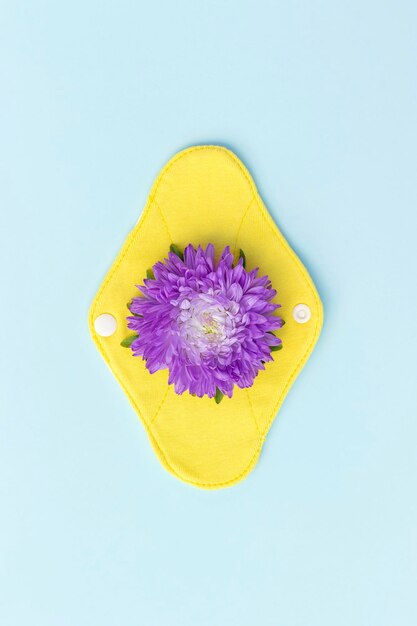 Bamboo charcoal washable sanitary napkin Yellow reusable menstrual pad on blue background with purple flower Health care and zerowaste no plastic ecofriendly concept