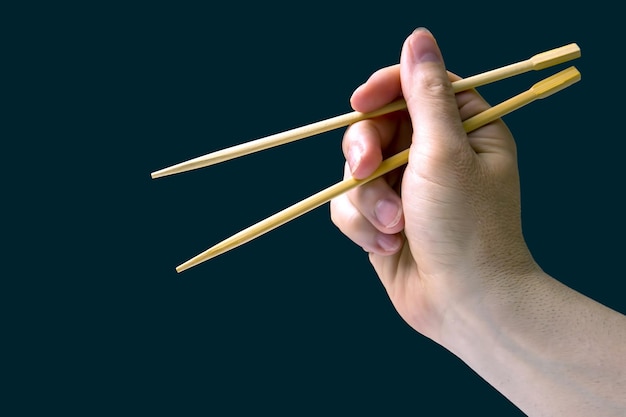 Bamboo chopsticks in a male hand on a dark background items for food