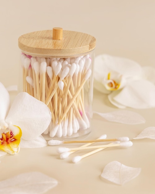 Bamboo cotton buds in a jar near white orchid flowers on light beige Eco friendly skincare product