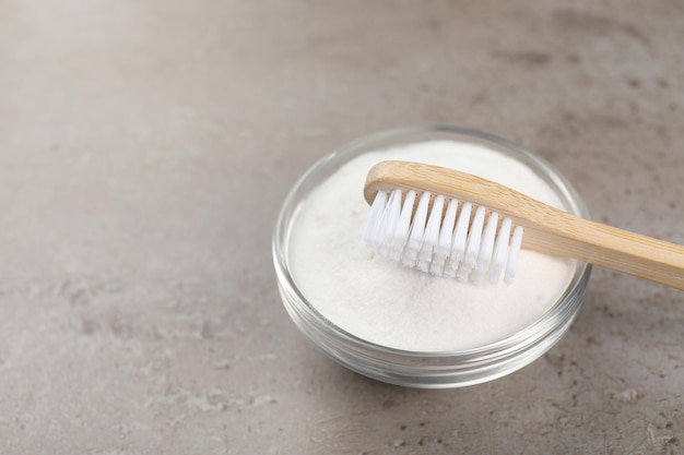 Bamboo toothbrush and bowl of baking soda on grey table Space for text