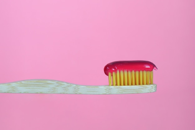 Bamboo toothbrush with paste highlighted on a pink background Dental care