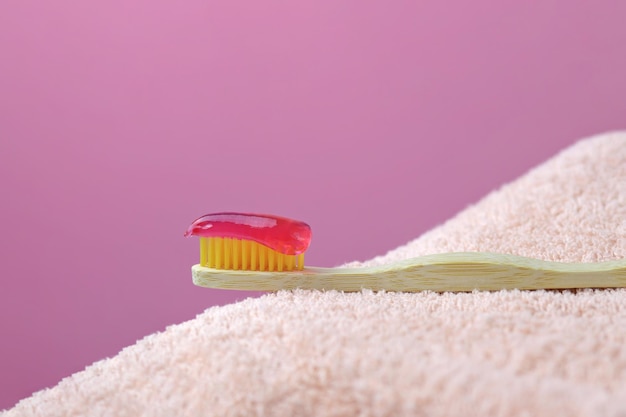 Bamboo toothbrush with pink paste on a towel Natural toothpaste on bamboo toothbrush pink backgrou