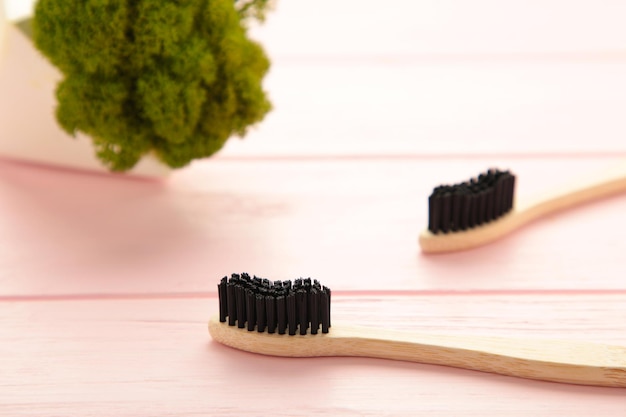 Bamboo wood toothbrush with black brush bristles on pink background