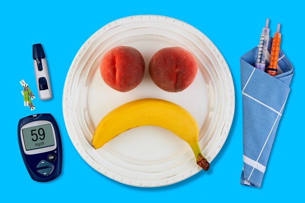 Banana and peach in the form of a sad smiley emoticon on a white plate and pen for insulin syringes