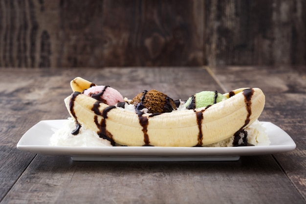 Banana split ice cream dessert with chocolate syrup on wooden