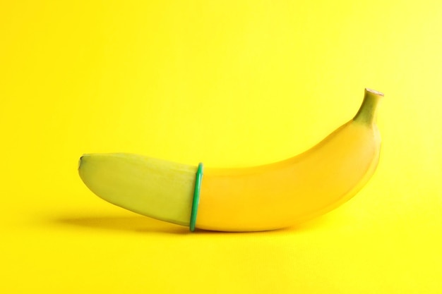 Banana with condom on yellow background