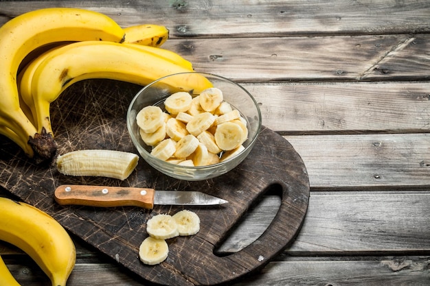 Bananas and banana slices in a plate on a black chopping Board with a knife